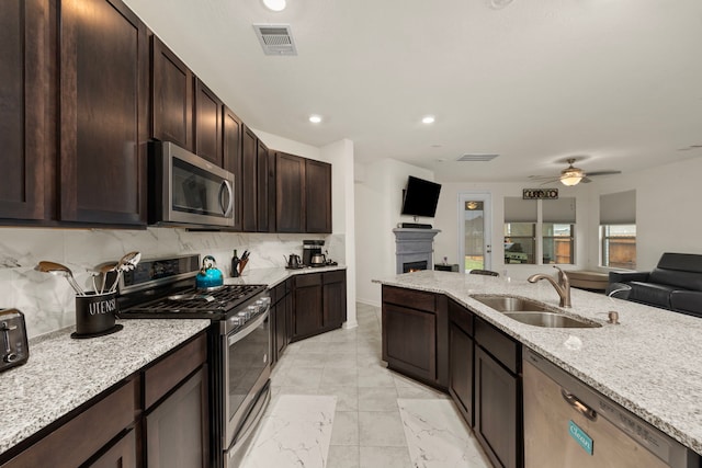 kitchen with dark brown cabinets, sink, stainless steel appliances, and light stone counters