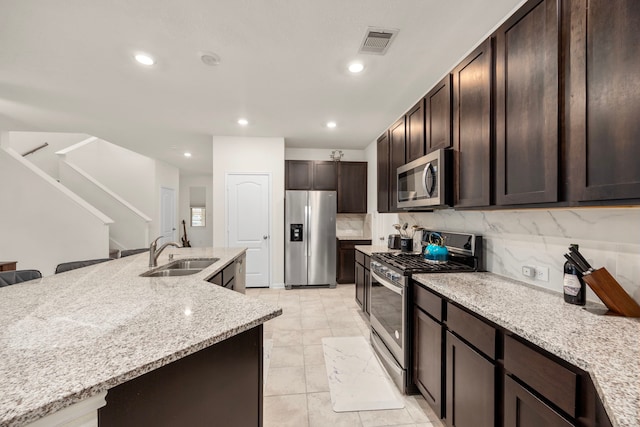 kitchen featuring light stone countertops, sink, appliances with stainless steel finishes, a breakfast bar area, and decorative backsplash