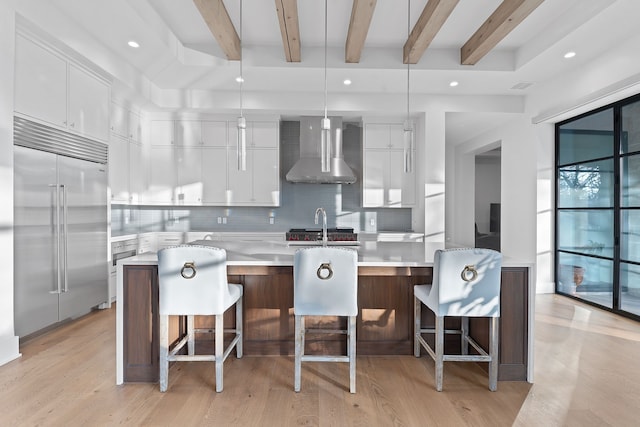 kitchen featuring white cabinets, wall chimney exhaust hood, a kitchen island, and built in refrigerator