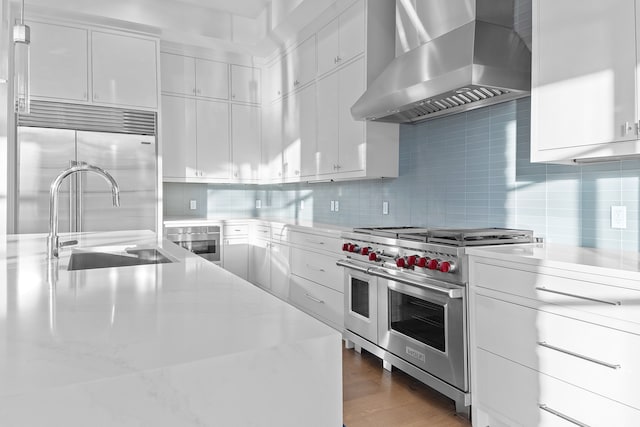 kitchen featuring exhaust hood, white cabinetry, high end appliances, and backsplash