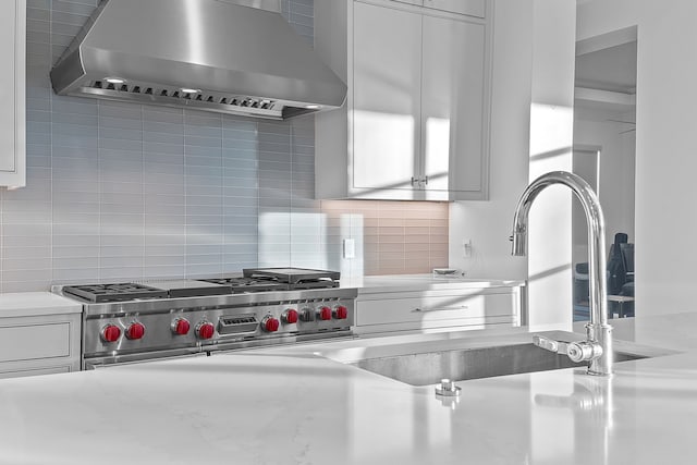 kitchen with tasteful backsplash, double oven range, white cabinetry, and range hood