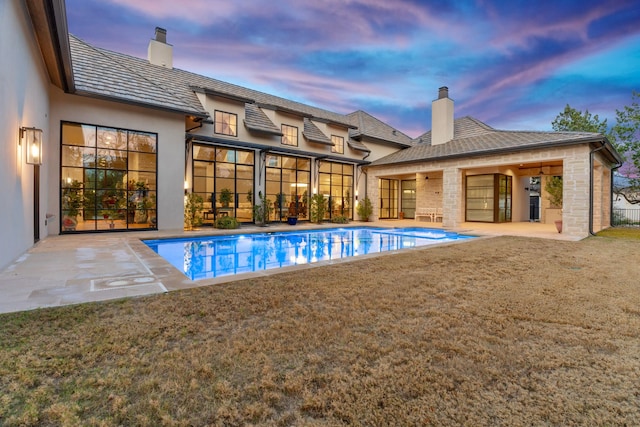 pool at dusk featuring a patio and a lawn