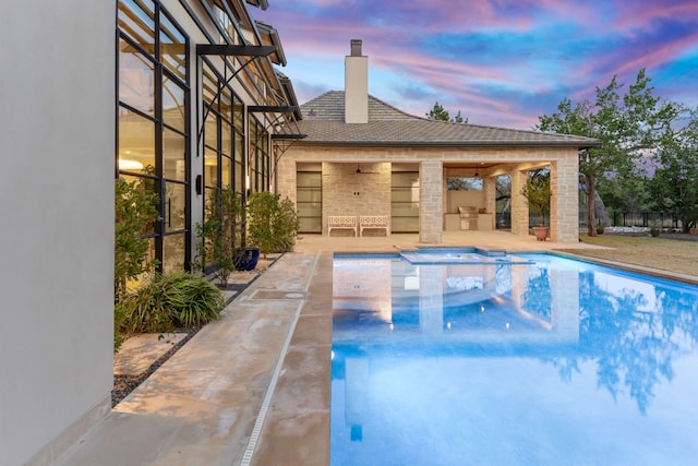 pool at dusk featuring an in ground hot tub, exterior kitchen, and a patio area