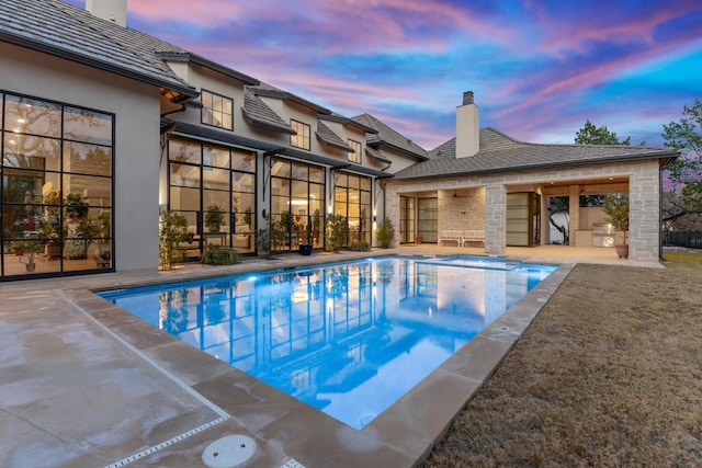 pool at dusk with area for grilling and a patio area