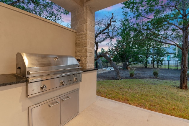 patio terrace at dusk featuring a yard, an outdoor kitchen, and grilling area