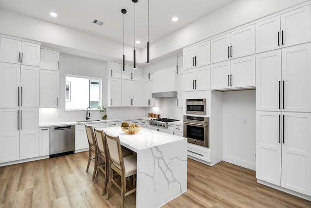 kitchen featuring white cabinets, stainless steel appliances, light stone counters, and a center island