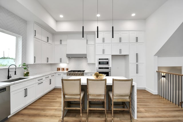 kitchen featuring appliances with stainless steel finishes, sink, a center island, pendant lighting, and wall chimney range hood