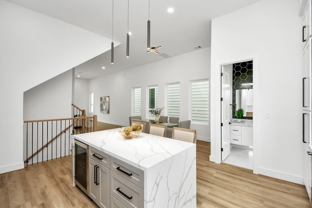 kitchen with white cabinetry, a center island, light hardwood / wood-style flooring, wine cooler, and light stone counters