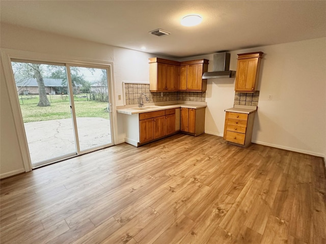 kitchen with sink, wall chimney exhaust hood, backsplash, and light wood-type flooring