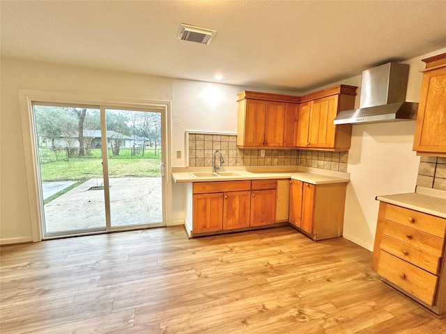 kitchen featuring sink, light hardwood / wood-style floors, wall chimney range hood, and backsplash