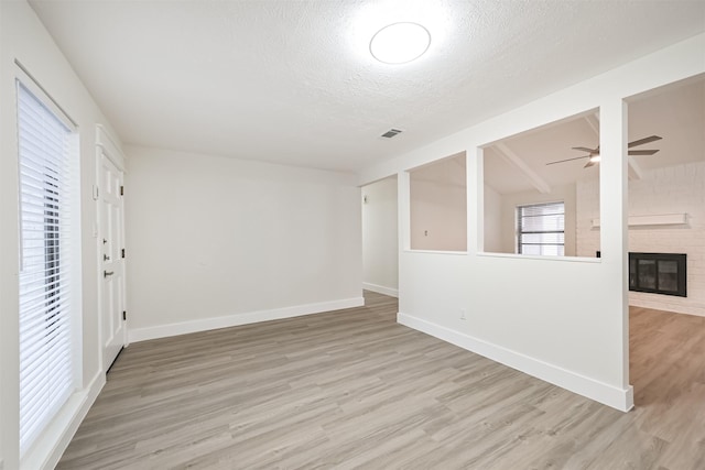 unfurnished room with a textured ceiling, ceiling fan, a fireplace, baseboards, and light wood-type flooring