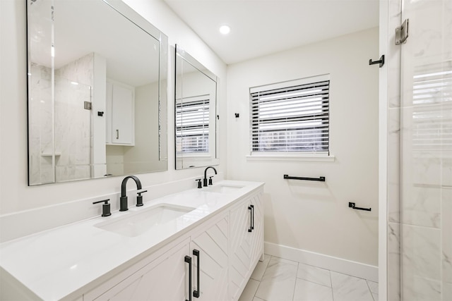 full bath with double vanity, a sink, a marble finish shower, and baseboards