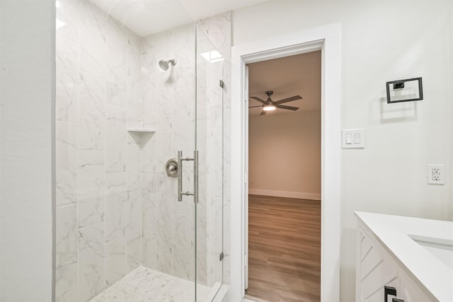 bathroom featuring a stall shower, ceiling fan, vanity, wood finished floors, and baseboards