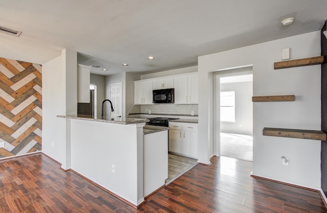 kitchen with dark stone countertops, white cabinetry, black appliances, and kitchen peninsula