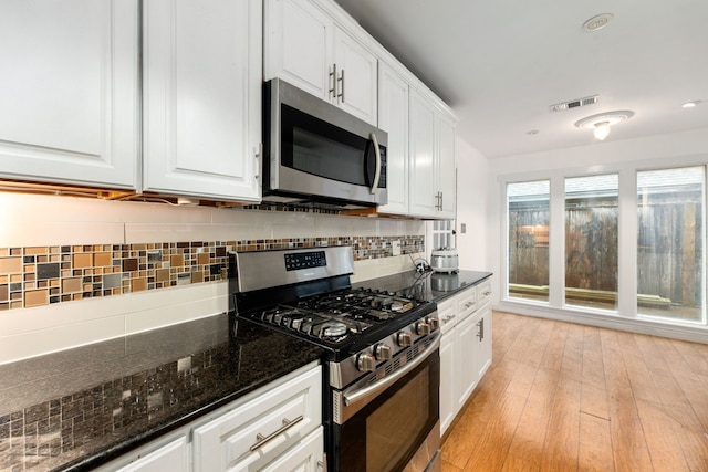 kitchen with white cabinetry, appliances with stainless steel finishes, dark stone countertops, and light hardwood / wood-style flooring