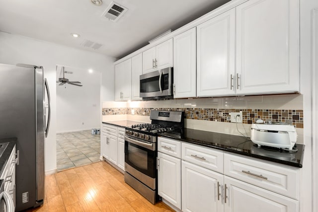 kitchen featuring dark stone countertops, appliances with stainless steel finishes, backsplash, light hardwood / wood-style floors, and white cabinets