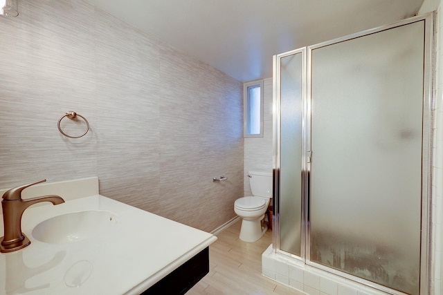 bathroom with a stall shower, tile walls, toilet, and vanity