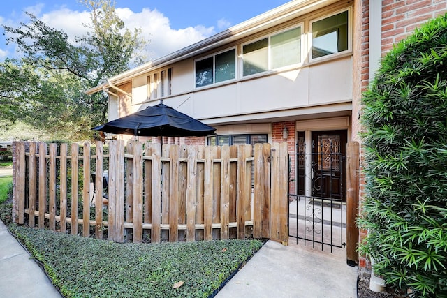 view of exterior entry with a gate, brick siding, fence, and stucco siding