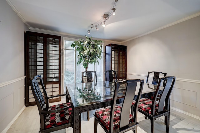 dining space with ornamental molding, rail lighting, wainscoting, and light wood-style flooring