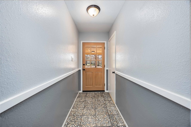 doorway with a textured wall and baseboards