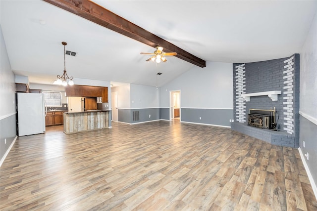 unfurnished living room featuring vaulted ceiling with beams, ceiling fan with notable chandelier, visible vents, baseboards, and light wood-type flooring