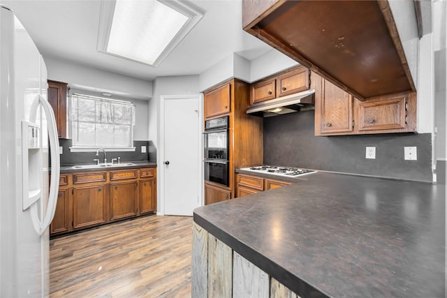 kitchen featuring dark countertops, white appliances, under cabinet range hood, and brown cabinetry