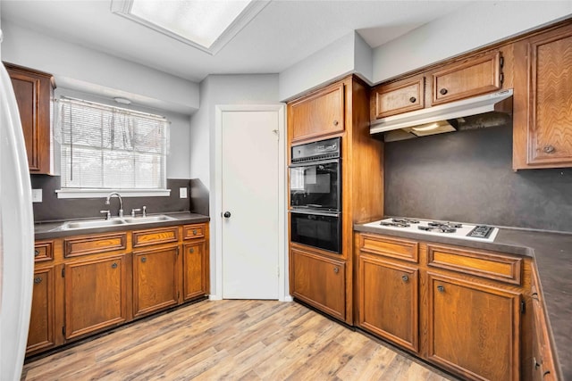 kitchen with brown cabinetry, dark countertops, under cabinet range hood, white gas cooktop, and a sink