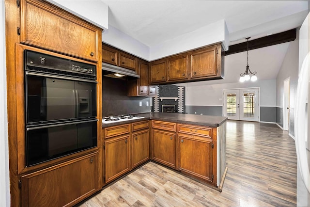 kitchen featuring under cabinet range hood, dobule oven black, white gas stovetop, a peninsula, and dark countertops