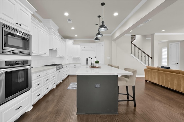 kitchen featuring a center island with sink, a breakfast bar area, open floor plan, stainless steel appliances, and white cabinetry