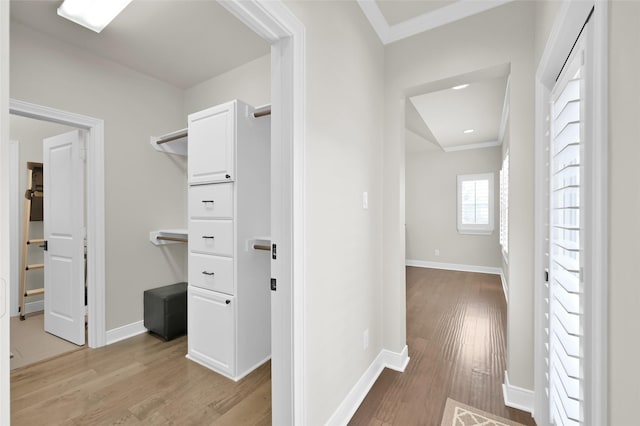 hall featuring baseboards, ornamental molding, and light wood-style floors