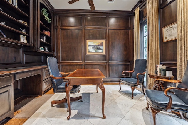 home office featuring light tile patterned floors, wooden walls, a decorative wall, a ceiling fan, and built in study area