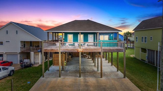 back house at dusk with a lawn, a porch, and a carport