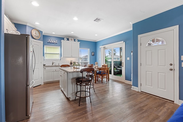 kitchen featuring white cabinetry, a kitchen island, stainless steel fridge, dark wood-type flooring, and a kitchen bar