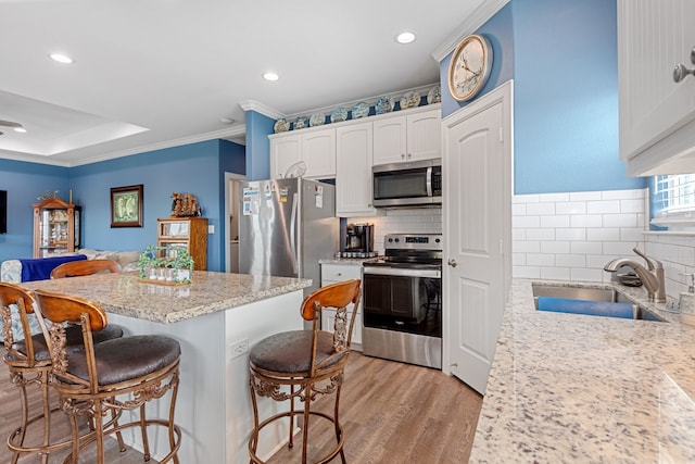 kitchen with a kitchen bar, white cabinetry, stainless steel appliances, and sink