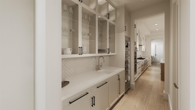 bar featuring light wood-type flooring, sink, black electric stovetop, white cabinets, and decorative backsplash