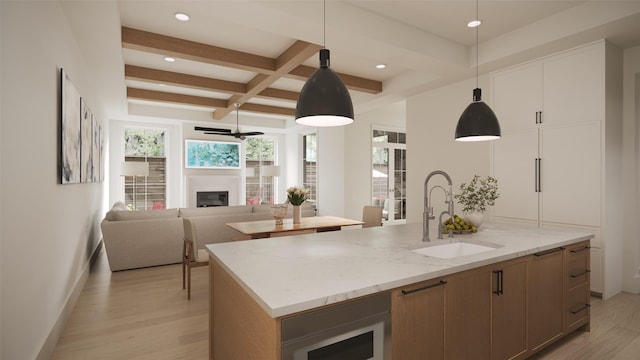 kitchen featuring sink, light wood-type flooring, pendant lighting, an island with sink, and light stone countertops