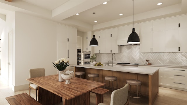 kitchen with hanging light fixtures, a kitchen breakfast bar, an island with sink, white cabinets, and sink