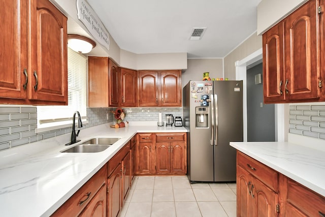 kitchen featuring sink, tasteful backsplash, light stone countertops, and stainless steel refrigerator with ice dispenser