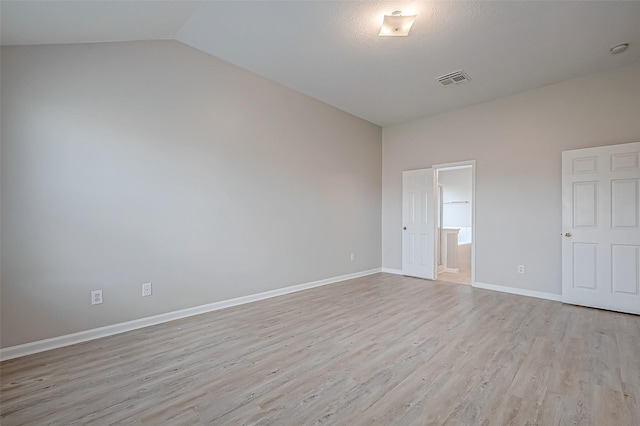 unfurnished bedroom with ensuite bathroom, light wood-style flooring, visible vents, baseboards, and vaulted ceiling