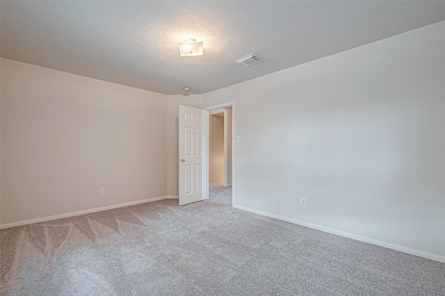 empty room featuring light colored carpet, visible vents, a textured ceiling, and baseboards