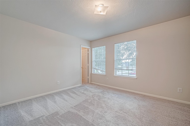 unfurnished room featuring light carpet, a textured ceiling, and baseboards