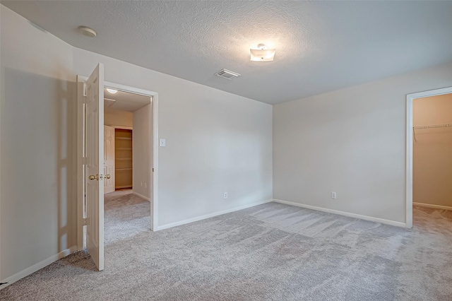 unfurnished room featuring a textured ceiling, baseboards, visible vents, and light colored carpet