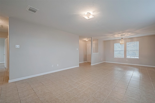 empty room featuring light tile patterned floors, a textured ceiling, visible vents, baseboards, and an inviting chandelier