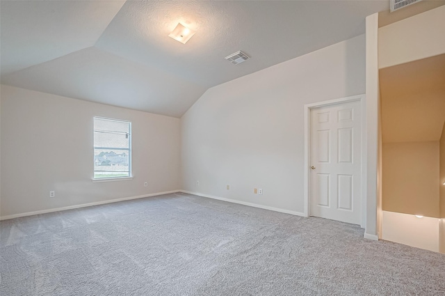 carpeted spare room featuring baseboards, visible vents, and vaulted ceiling