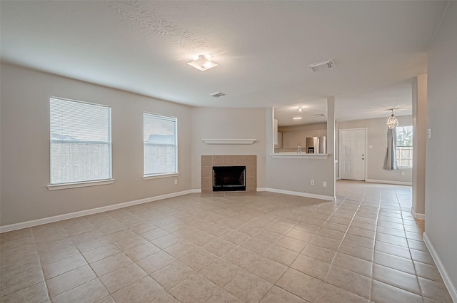 unfurnished living room featuring light tile patterned floors, a tiled fireplace, visible vents, and baseboards