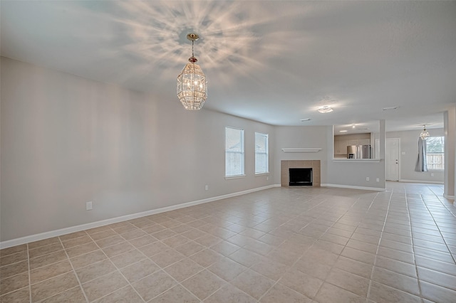 unfurnished living room featuring light tile patterned floors, a tiled fireplace, baseboards, and a notable chandelier