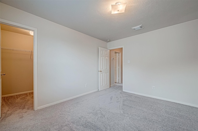 unfurnished bedroom featuring visible vents, a walk in closet, a textured ceiling, and light colored carpet