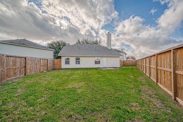 rear view of house with a fenced backyard, a chimney, and a lawn