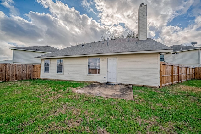 rear view of house with roof with shingles, a patio, a chimney, a lawn, and a fenced backyard