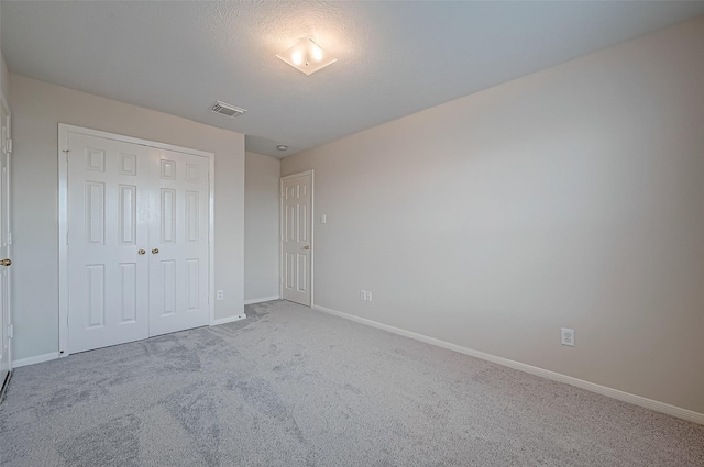 unfurnished bedroom with baseboards, visible vents, light colored carpet, a textured ceiling, and a closet